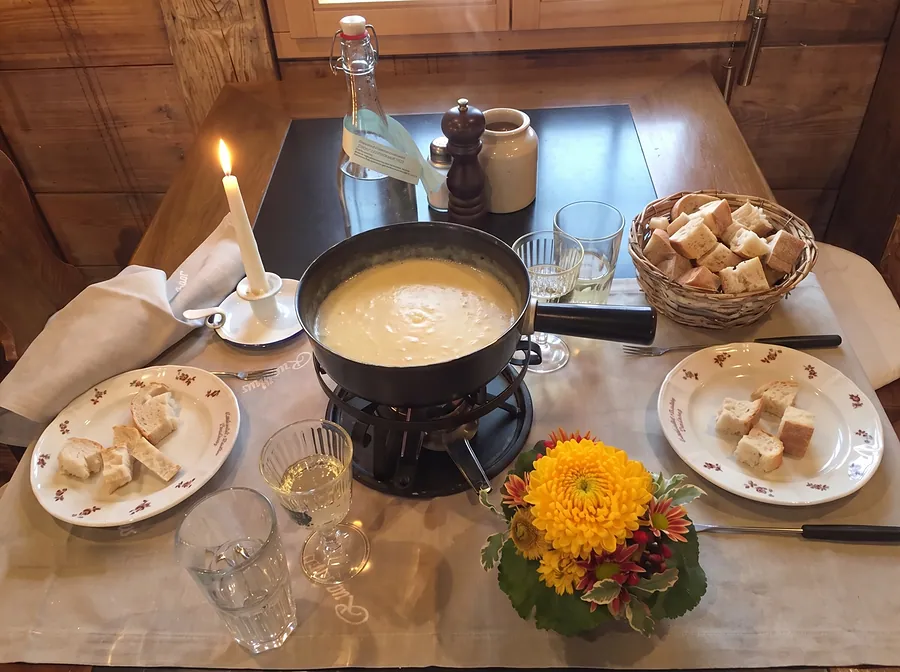 Fondue im Caquelon, Brot, Kerze und eine Herbstblume