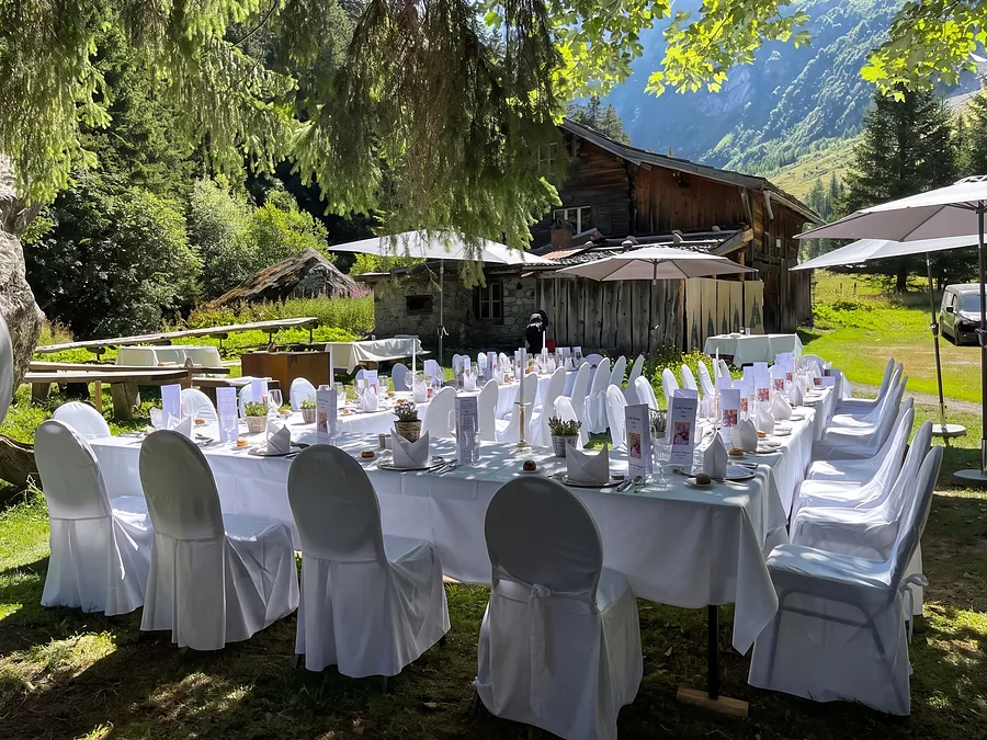 Weiss gedeckte Festtafel in der Wiese, dahinter das alte Holzhaus