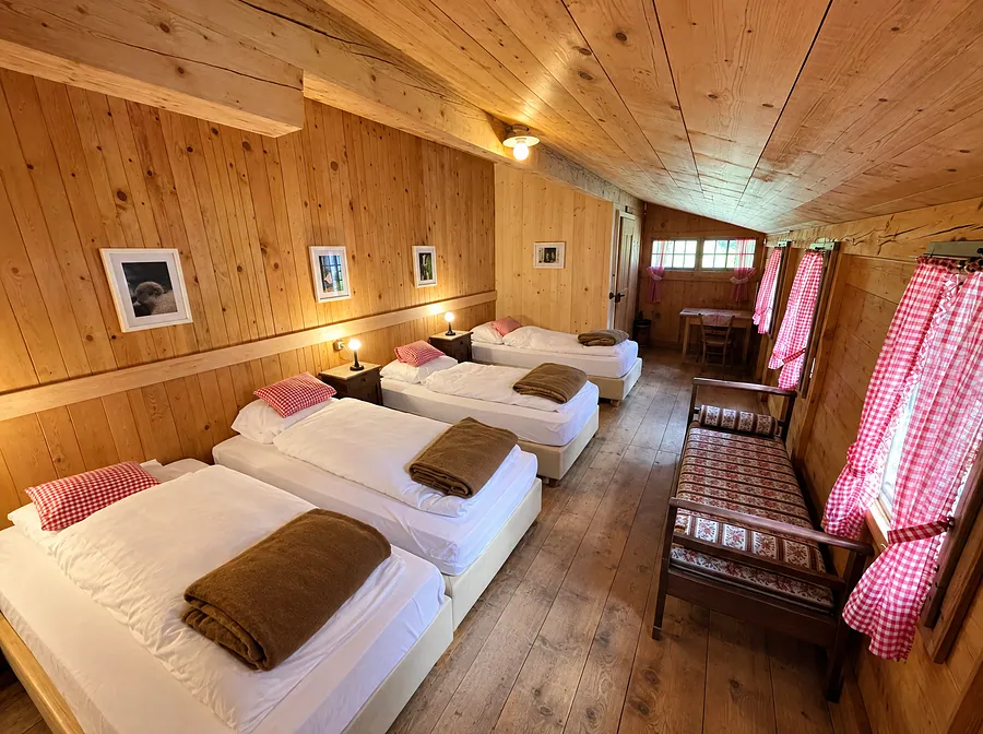 Langes Zimmer mit drei Betten und rot karierten Vorhängen